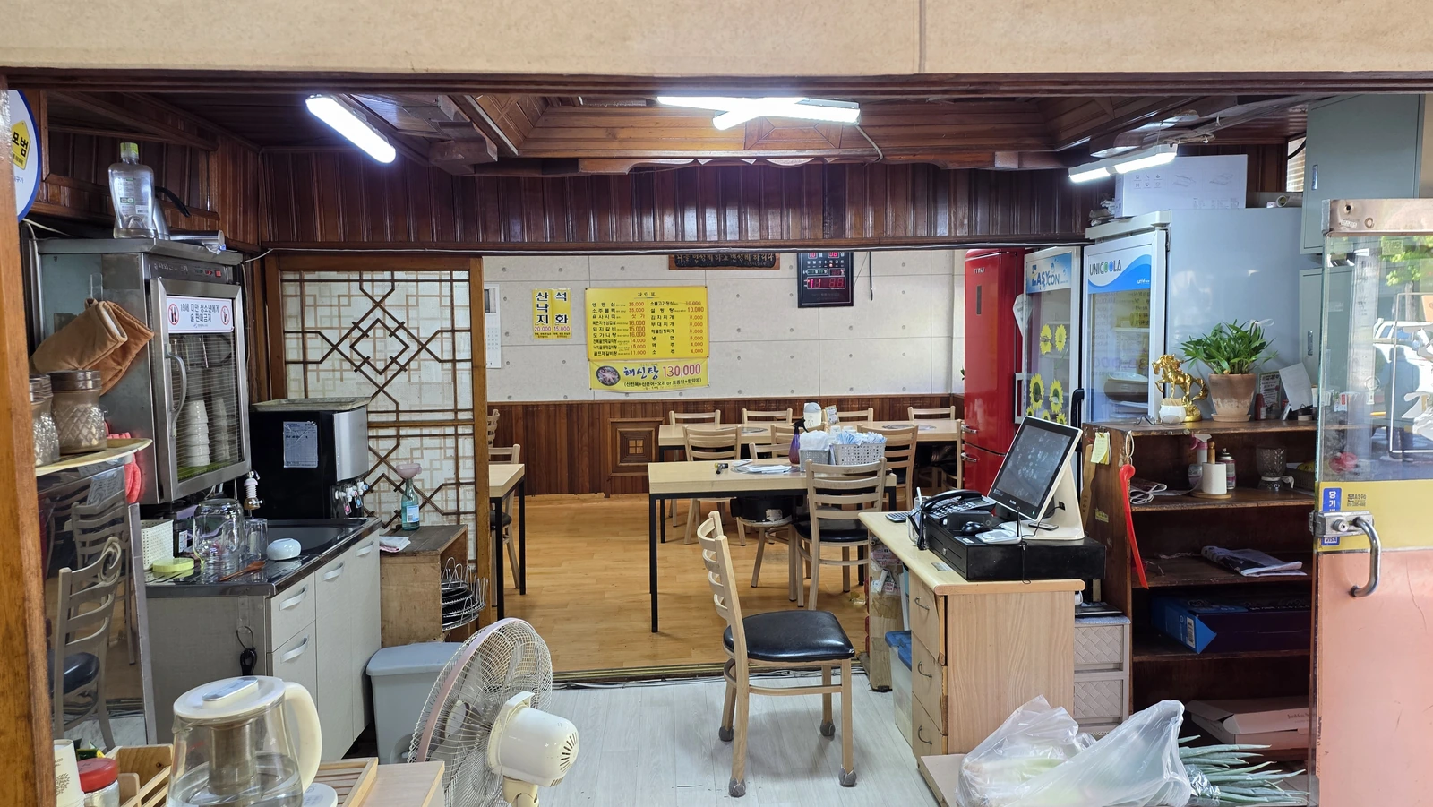 The restaurant interior from the entrance, with seats beyond a wooden door frame, a menu and the checkout counter
